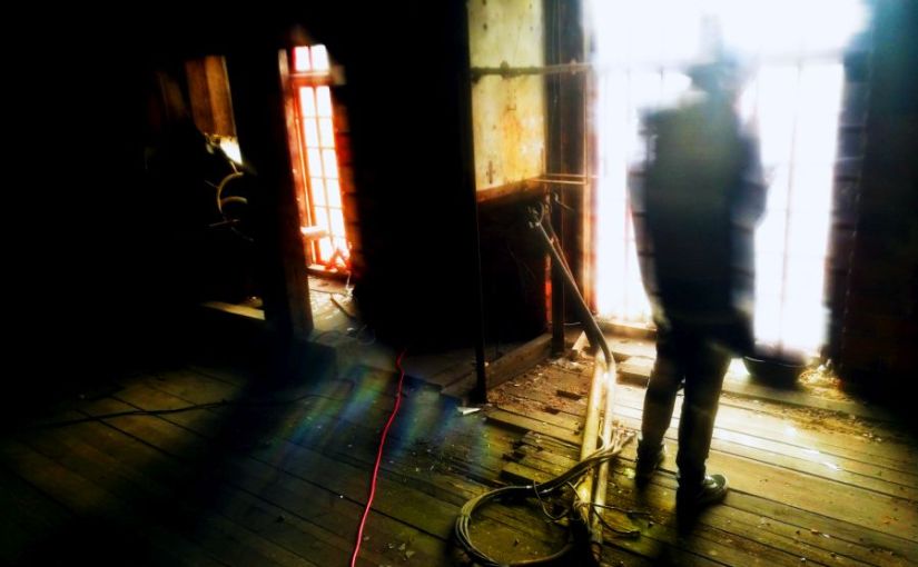 A person in silhouette against a large window in an abandoned room